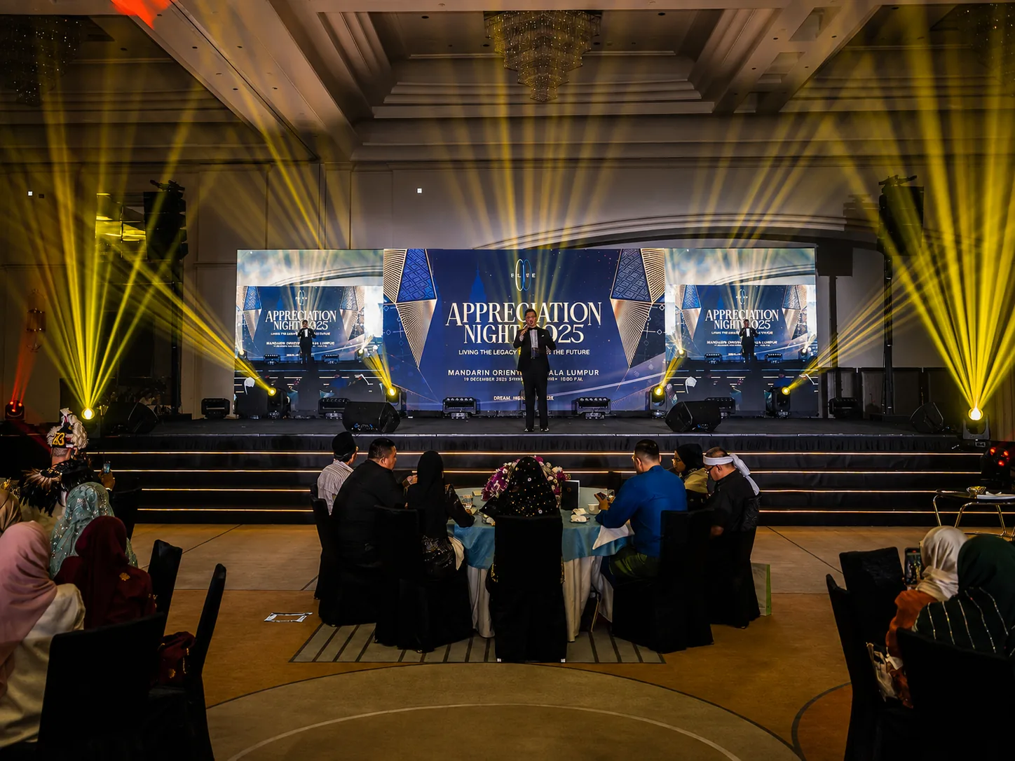 Appreciation Night 2025 at Mandarin Oriental – stage with wide LED screen and dramatic yellow beam lighting over gala tables